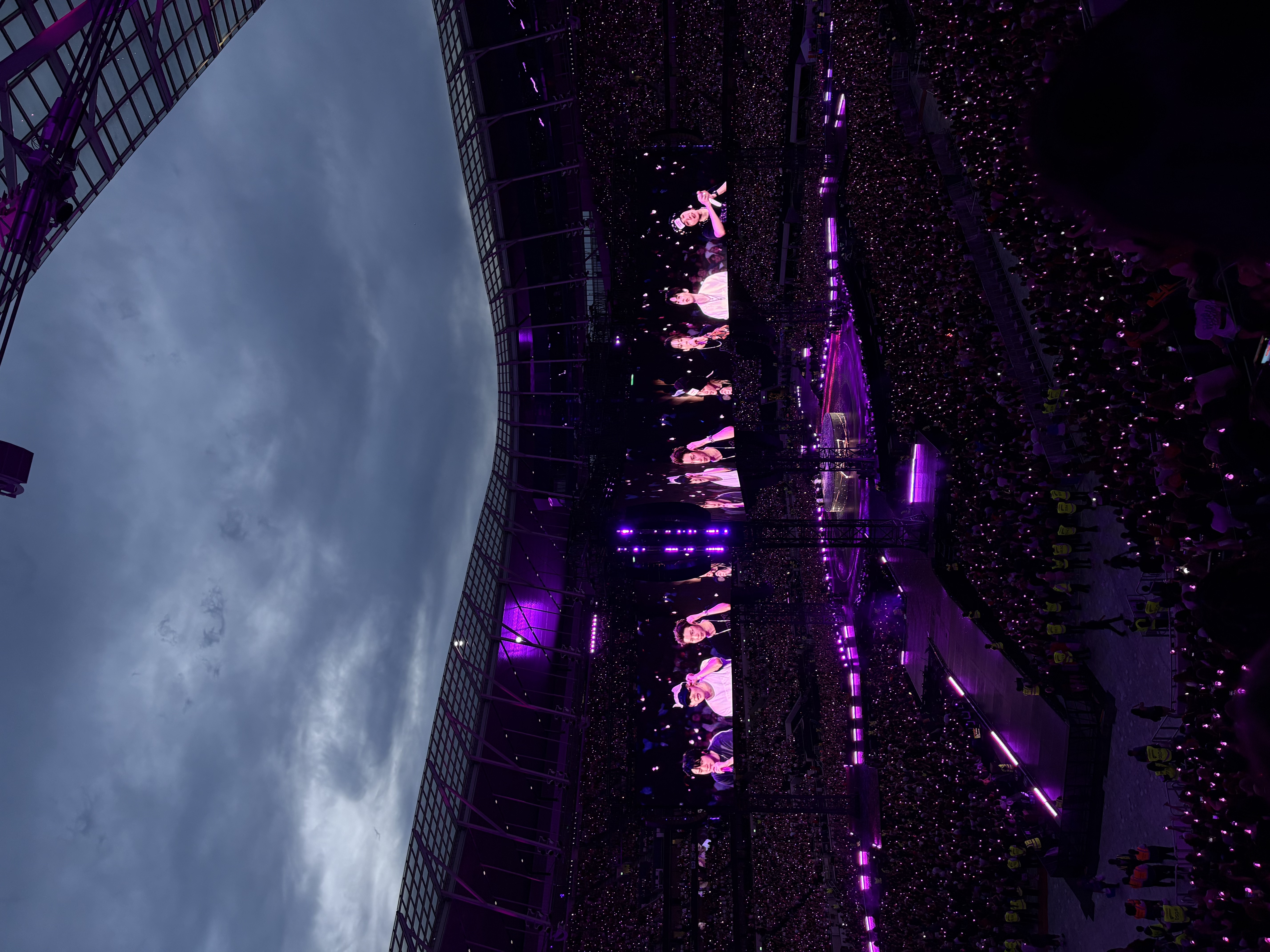 BTS performing beneath a dramatic stadium sky